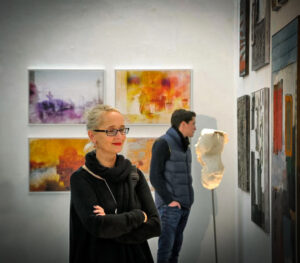 Zwei Besucher:innen betrachten im Gespräch farbige Arbeiten in einer Berliner Galerie