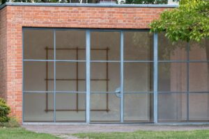 Installationsansicht Matt Browning A Screen of Trees im Mies van der Rohe Haus Berlin, Holzskulptur hinter der Glasfassade
