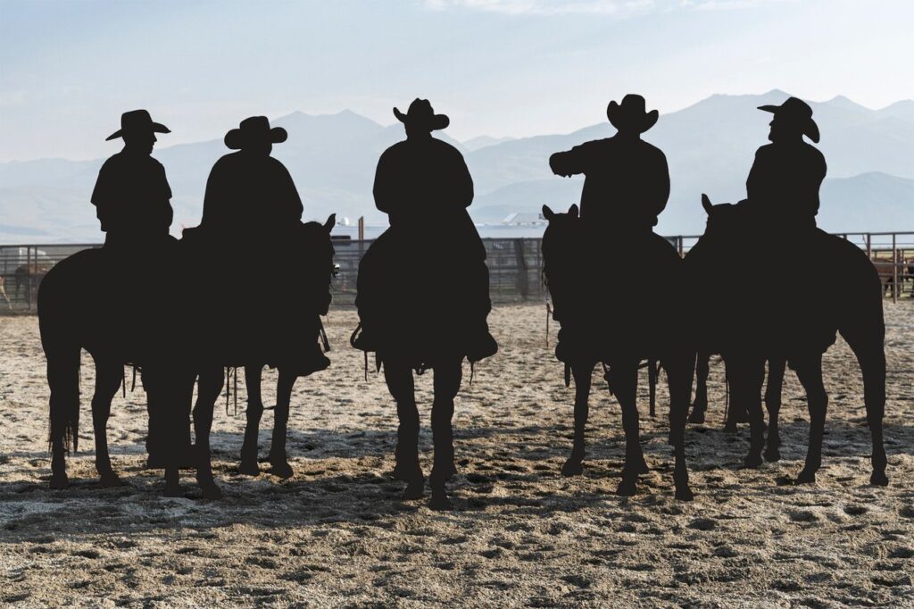 Ute Behrend HAUS#1: Silhouetten von fünf Cowboys zu Pferd in einer Rodeo-Arena vor Bergen