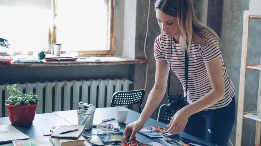 Eine Frau ordnet in einem Atelier mehrere Fotoabzüge auf einem Tisch